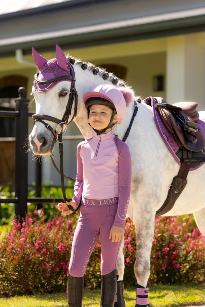 Young rider and grey pony wearing the LeMieux SS26 Fondant pastel pink collection, featuring a matching hat silk, base layer, and pony tack.